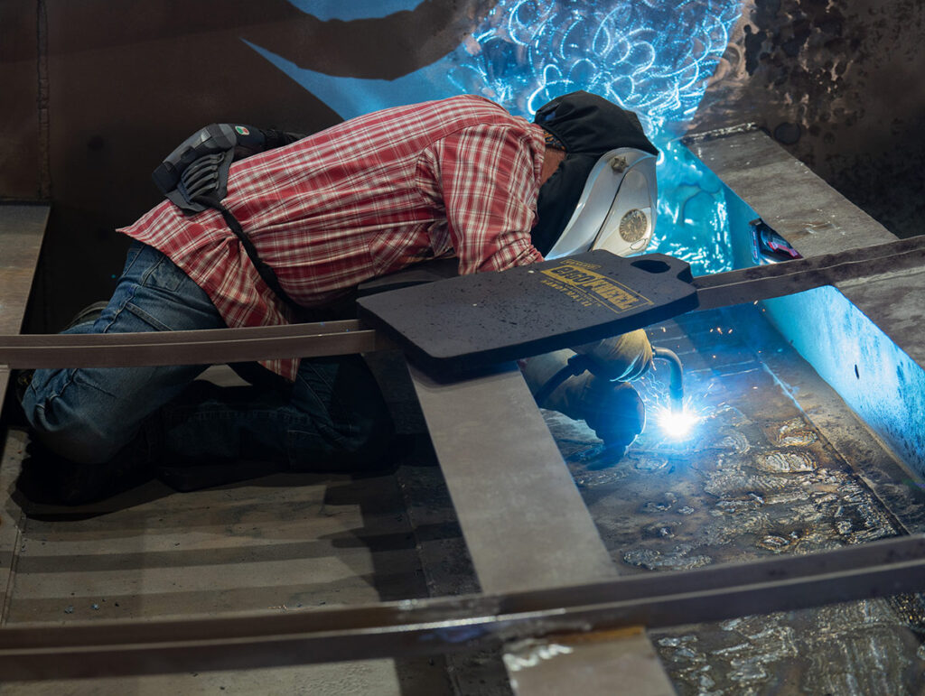 Millwright Mechanic repairs areas of corrosion on the back side of the Check 28 radial gate